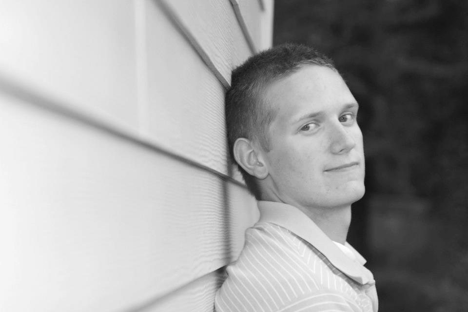 Black and white portrait of Daniel leaning against a white wall